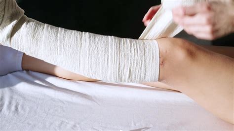 Woman After Knee Surgery Putting On Bandage On Couch Female Wearing