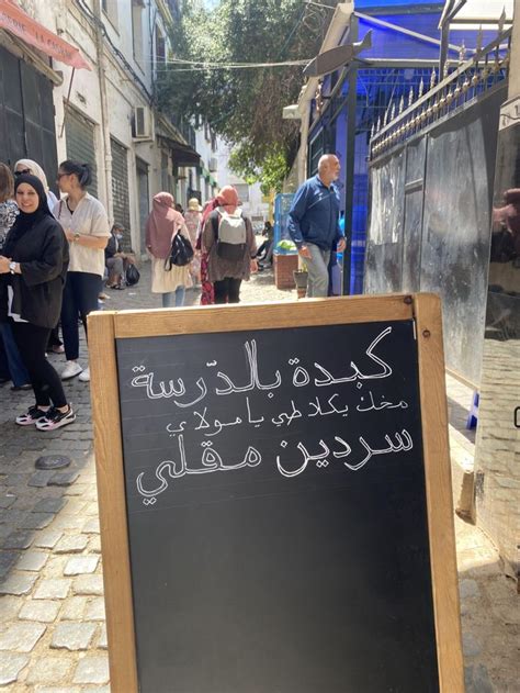 A Blackboard Sign With Writing On It In Front Of People Walking Down