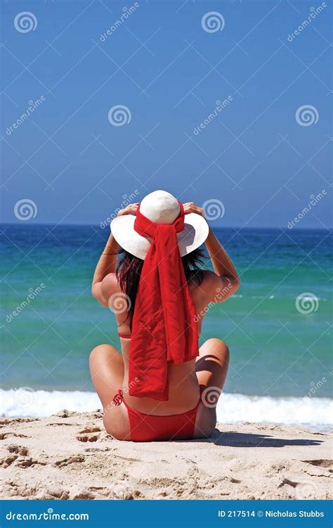 Mujer En El Bikiní Rojo Que Se Sienta En La Playa Que Ajusta El