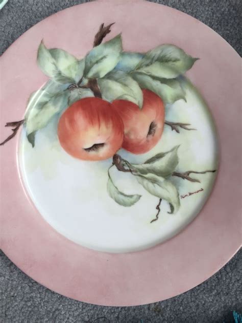 A Plate With Two Apples Painted On The Side And Leaves Around It