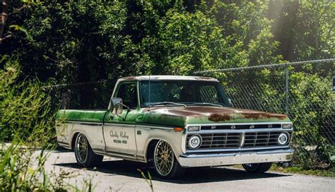 An Old Green And White Truck Parked On The Side Of A Road Next To Trees