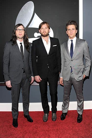 Three Men In Suits Standing On A Red Carpet