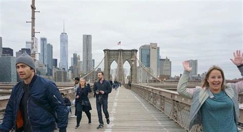 People Walking Across A Bridge In Front Of The City Skyline With Their