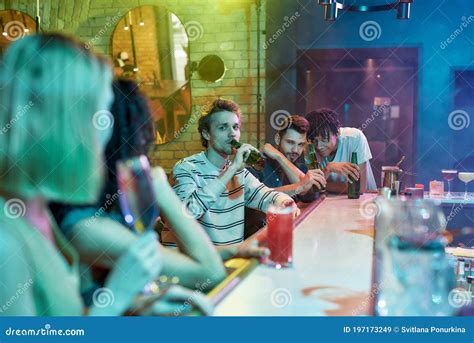 Three Guys Drinking Beer Flirting Looking At Women Sitting At The Bar