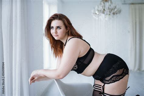 A Plus Size Model In Lacy Black Lingerie Poses In A Bright Room With A