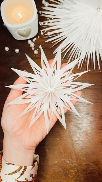 Someone Is Holding Some Paper Snowflakes On A Table Next To A Lit Candle