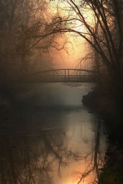 A Bridge That Is Over Some Water In The Foggy Day With Trees On Both Sides