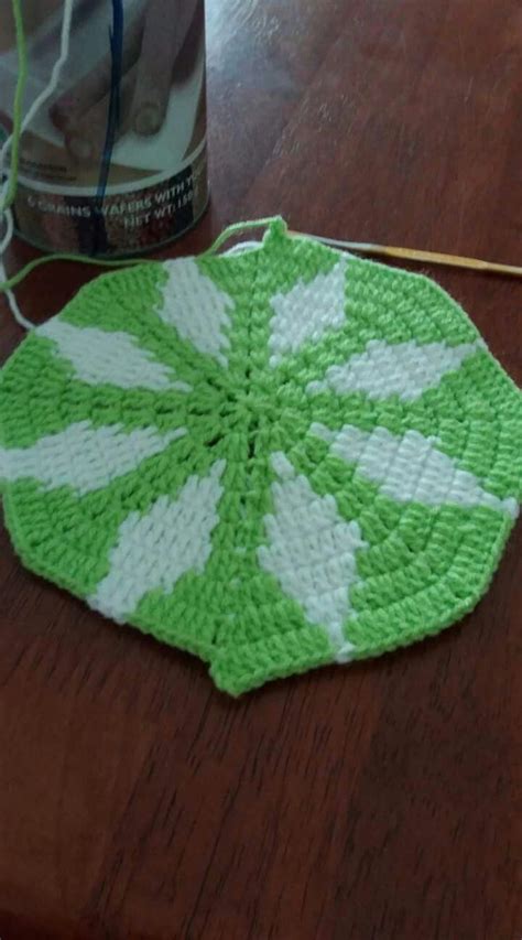 A Green And White Crocheted Doily Sitting On Top Of A Wooden Table