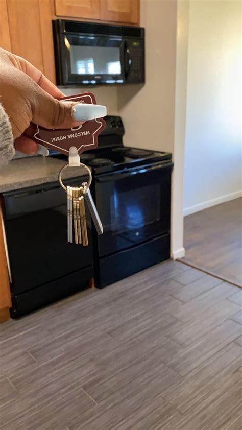 A Person Holding A House Key In Front Of A Kitchen With Black Stove And