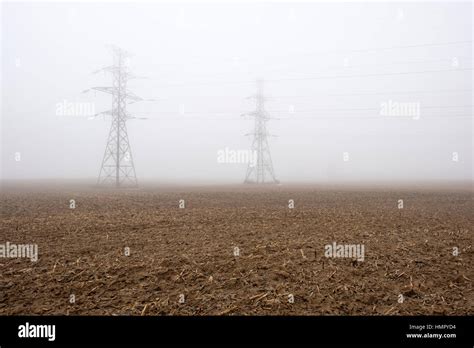 Two Power Line Towers Pylons In A Farm Field Under Heavy Fog In