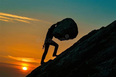 Silhouette Of A Man Pushing A Boulder On A Mountain At Sunset Stock