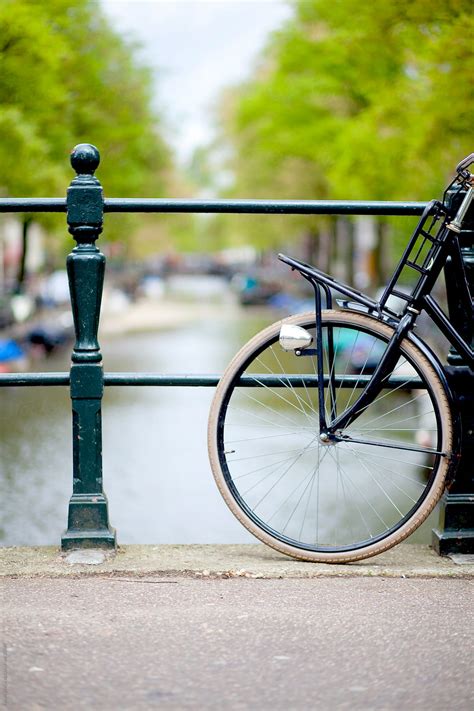 "A Classic Bike Standing On A Bridge With An Amsterdam Canal, Trees And