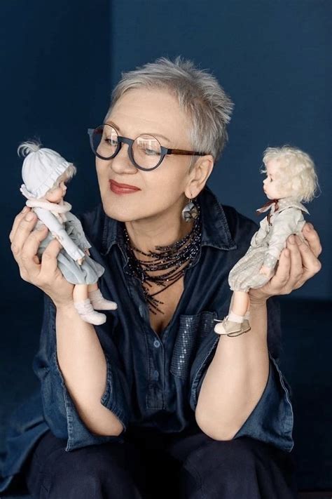 An Older Woman Holding Two Small Dolls In One Hand And Looking At The