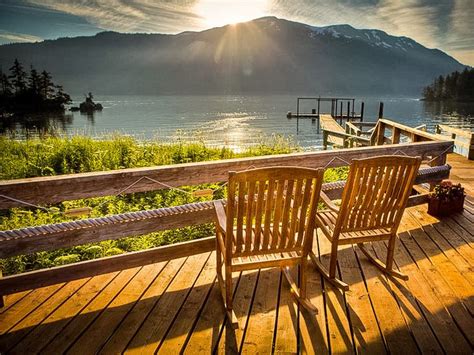 Two Wooden Chairs Sitting On Top Of A Wooden Deck Next To A Body Of Water