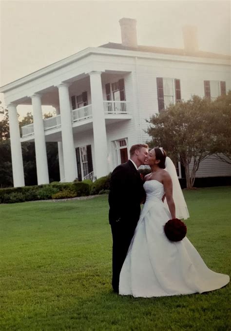 A Bride And Groom Kissing In Front Of A Large White House