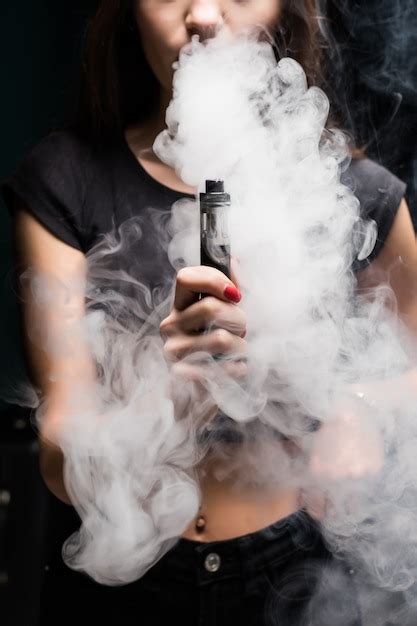 Free Photo Young Sexy Woman Is Vaping Smoking E Cigarette Cloud Of Vapor On The Black Wall