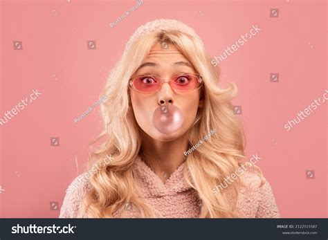 Joyful Blonde Lady Chewing Gum And Blowing Bubble Looking At Camera On Pink Studio Images
