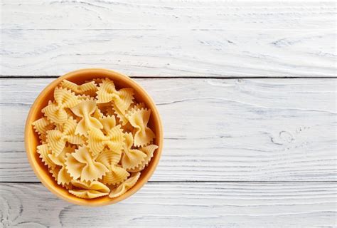 Pasta farfalle rigate sin cocer en un tazón de madera sobre fondo