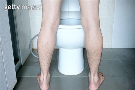 Rear View Leg Of Man Standing Peeing To Toilet Bowl In Restroom At Home