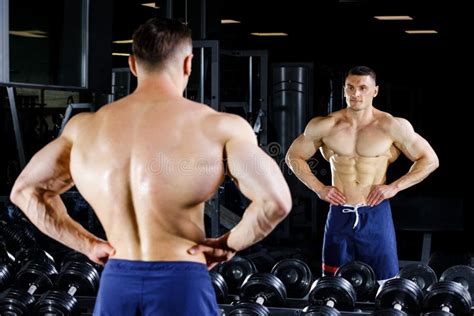 Young Bodybuilder With Great Muscles Posing In Gym Before The Mirror