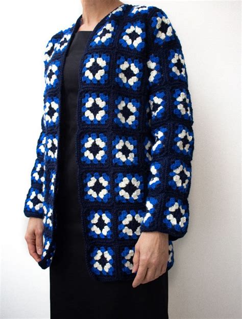 A Woman Wearing A Blue And White Crochet Jacket Standing Next To A Wall