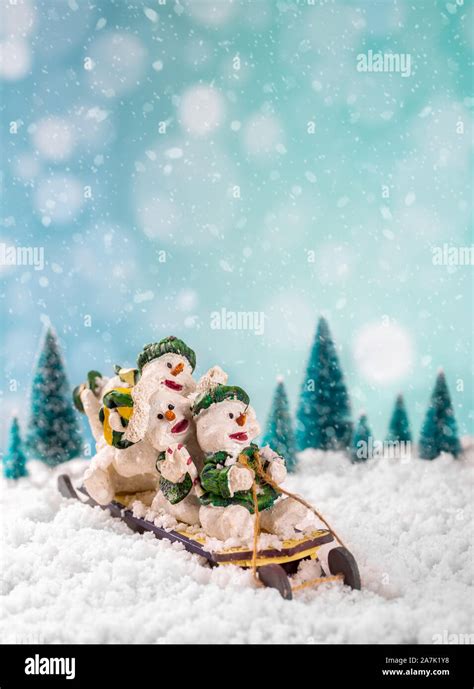 Winter Scene Of Snowmen Figurines On A Sled With Falling Snow On A