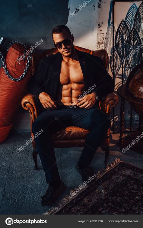 Brutal Hipster With Naked Torso Posing On Chair In Room Stock Photo