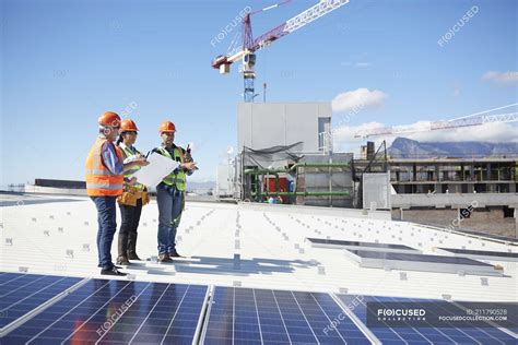 Engineers With Blueprint At Solar Panels At Sunny Power Plant