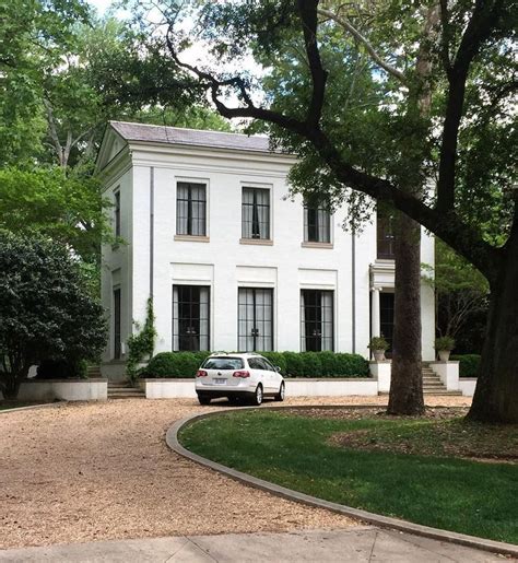 A Car Parked In Front Of A Large White House With Lots Of Trees And Bushes