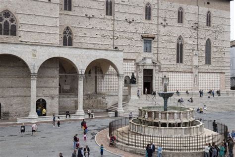 People Are Gathered Around A Fountain In Front Of An Old Building