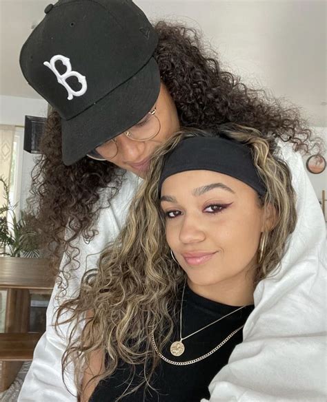 Two Women With Curly Hair And One Wearing A Baseball Cap Both Looking