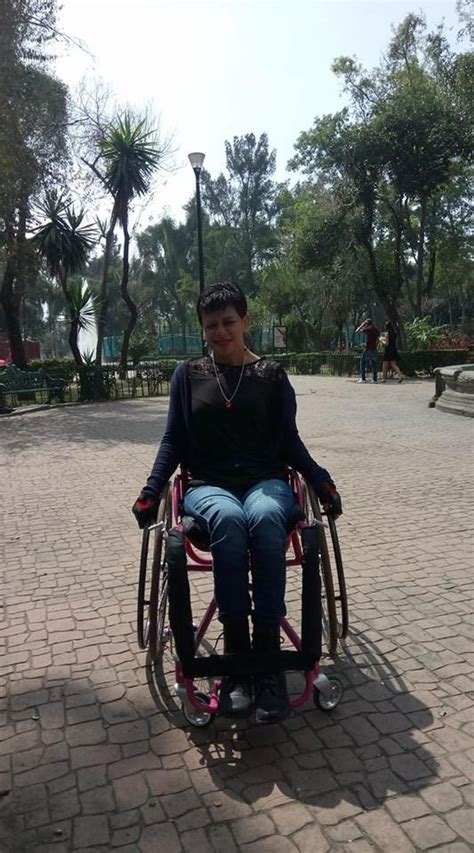 A Woman Sitting In A Wheel Chair On A Brick Walkway With Trees And