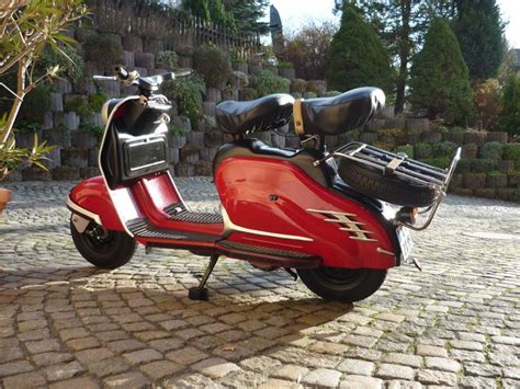 A Red Scooter Parked On Top Of A Cobblestone Road Next To A Tree