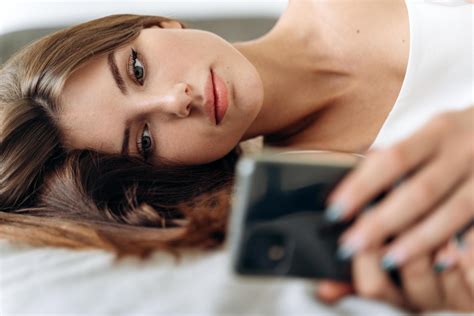 Woman Looking At Mobile Phone While Laying On Her Bed Stock