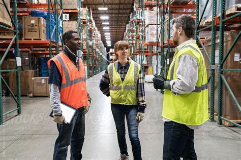 Three Workers Wearing Safety Vests Having A Discussion In A Distribution Center Safety Vest