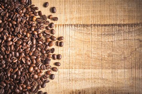 Granos de café tostados derramados sobre fondo de mesa de madera Foto