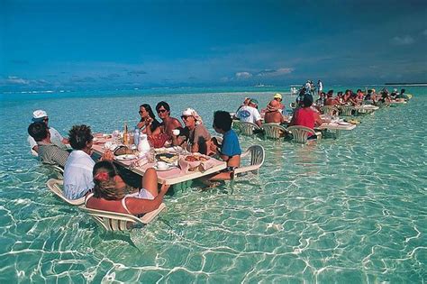 A Group Of People Sitting At A Table In The Ocean Eating Food And