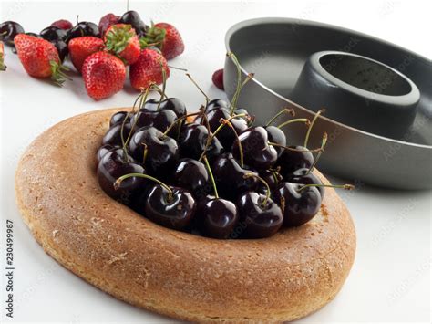 Bizcocho savarín relleno de cerezas junto a un molde redondo y frutas