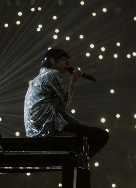 A Man Sitting On Top Of A Piano In Front Of A Stage With Lights Behind Him