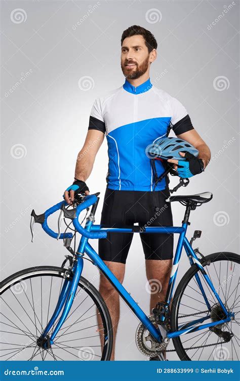 Professional Bearded Cyclist With Helmet And Bicycle Standing In Studio