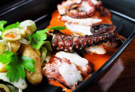 an octopus is served with potatoes and carrots on a black plate, along ...