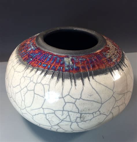 A White Vase With Red Blue And Orange Designs On The Inside Is Sitting