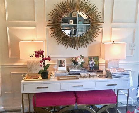 A White Desk Topped With A Mirror And Two Pink Stools Next To A Vase