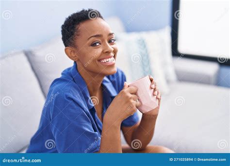 African American Woman Drinking Coffee Sitting On Sofa At Home Stock