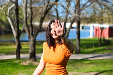 Pretty Young Woman Brunette And Orange Dress Puts Her Hand In Front Of Her Face To Protect