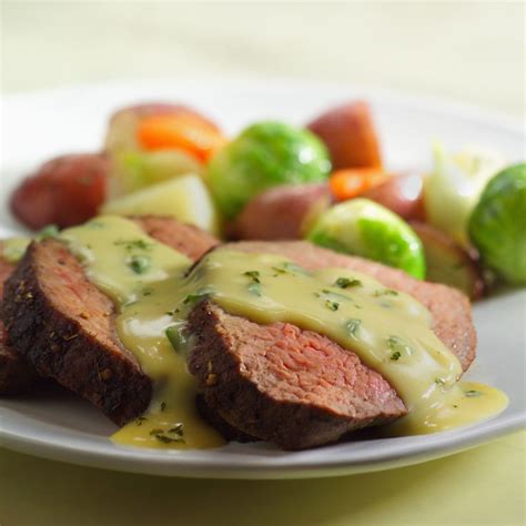 A White Plate Topped With Meat Covered In Gravy Next To Veggies