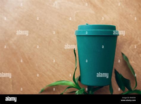 Stylish Reusable Eco Coffee Cup And Bamboo Leaves On Wooden Background