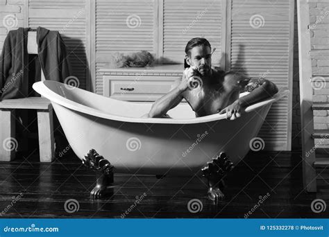 Macho Sitting Naked In Bathtub Washing With Sponge Man With Beard And Thoughtful Face Taking
