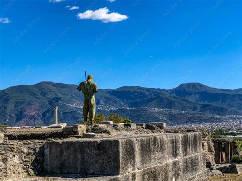 Back View Of A Naked Bronze Sculpture At The Roman Ruins Of Pompeii In Italy Under A Blue Sky