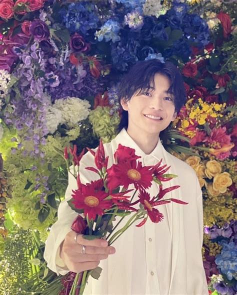 A Person Holding Flowers In Front Of A Flower Wall